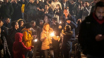 Silvester in Köln: Eine Menschengruppe beobachtet Feuerwerk, im Vordergrund stehen Menschen und halten Wunderkerzen.