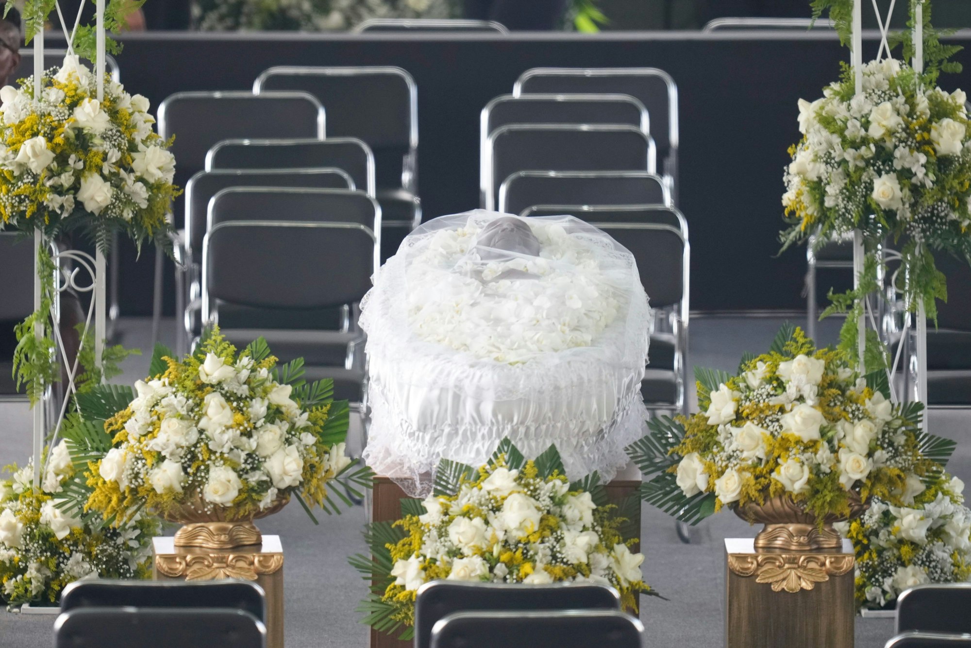 Auf einem Podest steht der Sarg von Pele, beschmückt mit weißen Blütenblättern und einem Gewand.