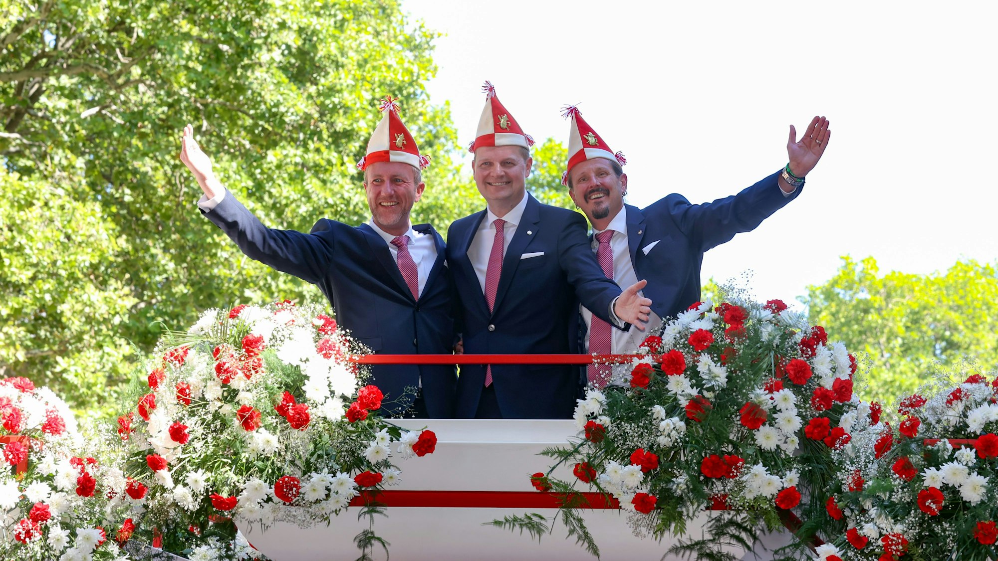 Bei der Vorstellung des designierten Kölner Dreigestirns 2023
sind André Fahnenbruck , Boris Müller und Marco Schneefeld zu sehen. Sie stehen einigen Blumen und halten die Arme in die Luft.