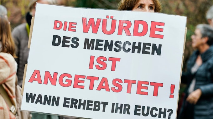 Eine Frau hält in einer Protest-Demonstration in Weinheim (Baden-Württemberg) ein Plakat in den Händen, auf dem steht: „Die Würde des Menschen ist angetastet! Wann erhebt ihr euch?“