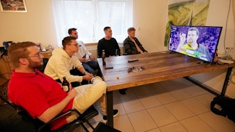 Fünf junge Männer schauen ein Spiel der Darts-WM von Gabriel Clemens im Fernseher an.