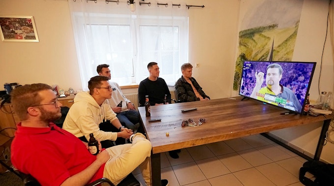 Fünf junge Männer schauen ein Spiel der Darts-WM von Gabriel Clemens im Fernseher an.
