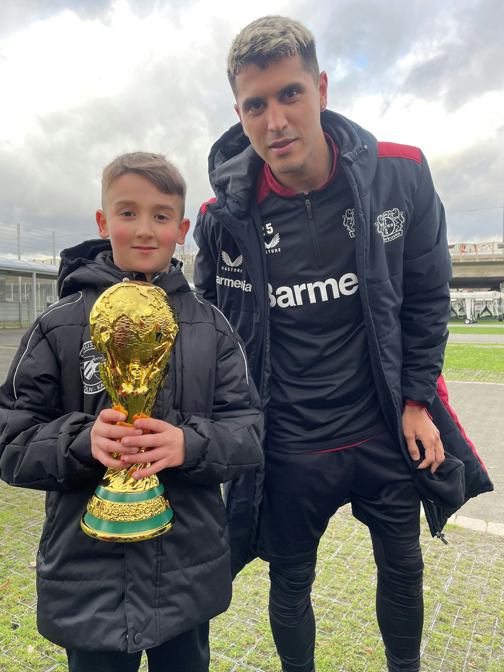 Bayer-Fan Cebrail Turgut begrüßt Exequiel Palacios mit seinem eigenen WM-Pokal