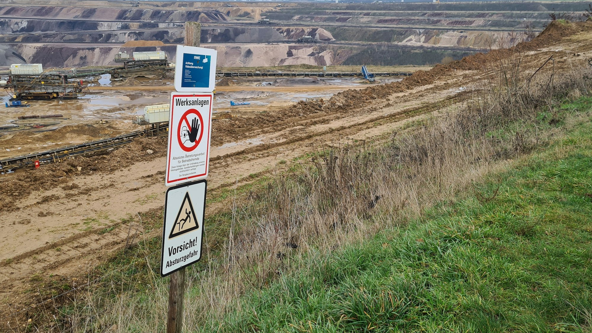 Der Tagebau Garzweiler. Im Vordergrund stehen Schilder, die zur Vorsicht mahnen.