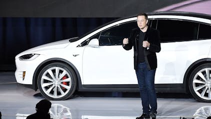 Elon Musk spricht auf einer Bühne im September 2015 zur Einführung des Tesla X. Im Hintergrund ist ein weißes Exemplar des Autos zu sehen.