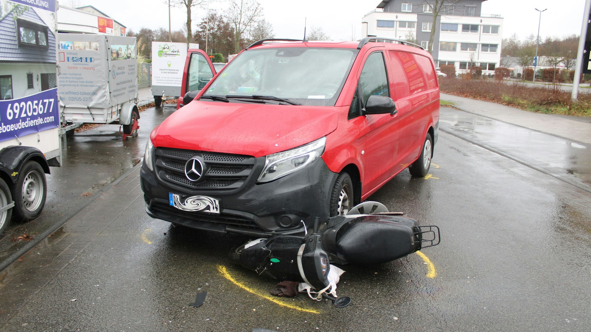 Ein Roller ist unter einem roten Mercedes-Transporter eingeklemmt.