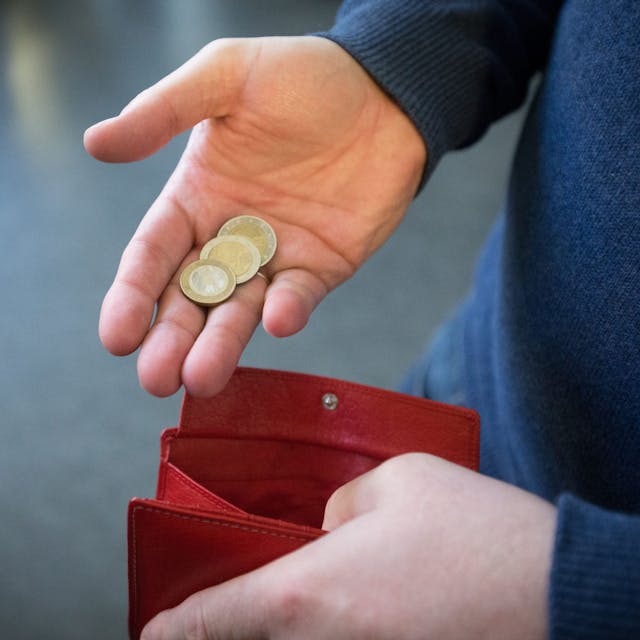 ILLUSTRATION - 31.01.2017, Nordrhein-Westfalen, Paderborn: ARCHIV - Münzen im Wert von fünf Euro liegen in einer Hand über einem Portemonnaie.&nbsp;