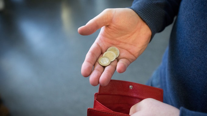 ILLUSTRATION - 31.01.2017, Nordrhein-Westfalen, Paderborn: ARCHIV - Münzen im Wert von fünf Euro liegen in einer Hand über einem Portemonnaie.&nbsp;
