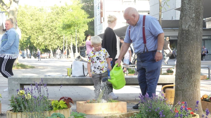 Streetworker Antonio Pizzulli steht mit einem kleinen Jungen in der Bocklemünder Fußgängerzone und gießt dort selbst angelegte Blumenbeete.