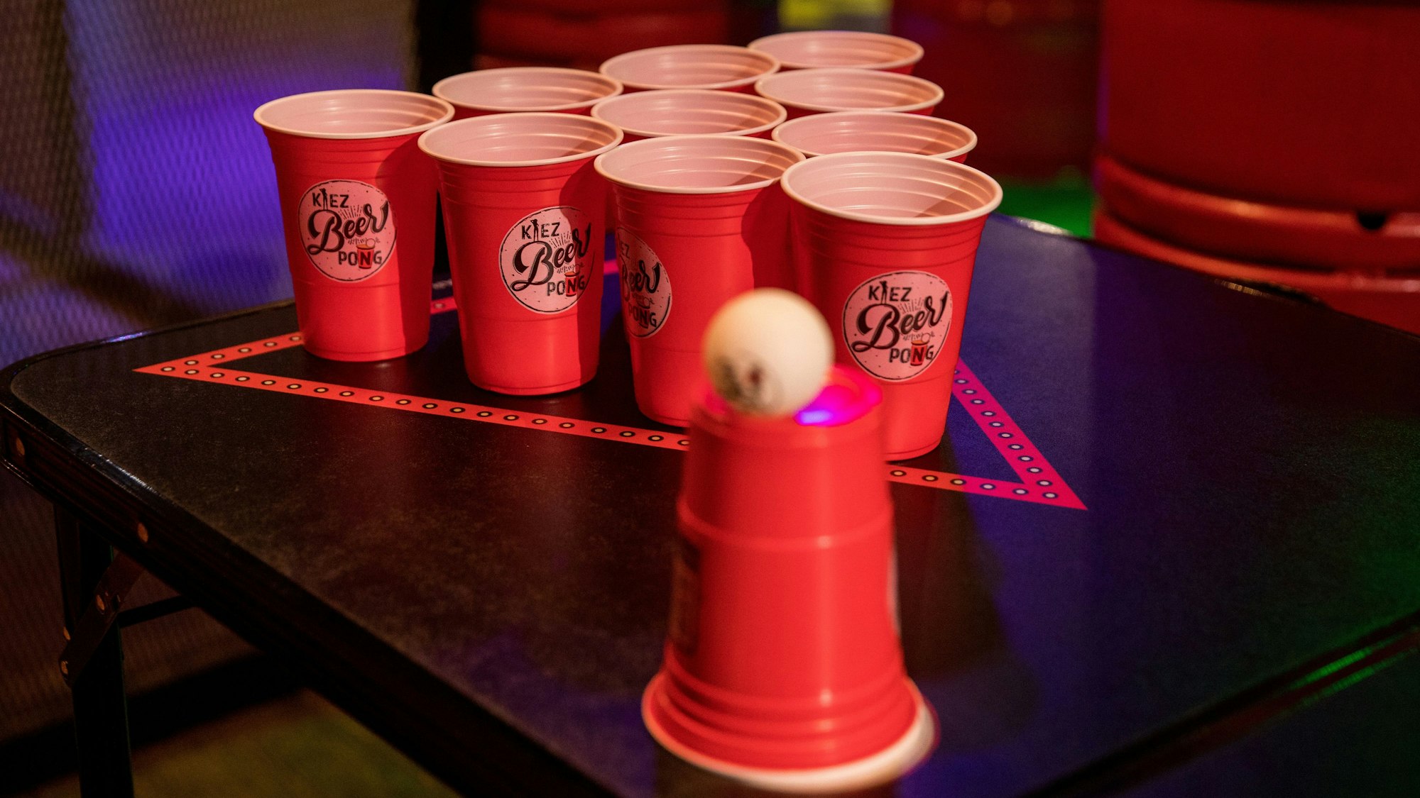 Rote Becher auf einem Tisch, dazu ein Tischtennisball, das Set für das Spiel Beerpong.
