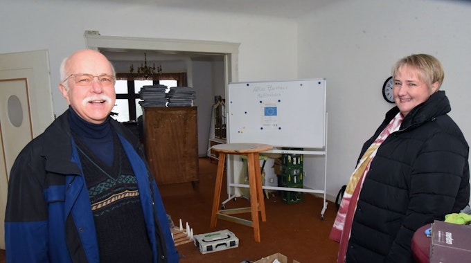 Anke Bockelmann und Georg-Wilhelm Overbeck stehen in einem der renovierungsbedürftigen Räume des Pfarrhauses in Marienheide-Müllenbach. Im Hintergrund sind weggerückte Schränke und gepackte Kartons zu sehen.