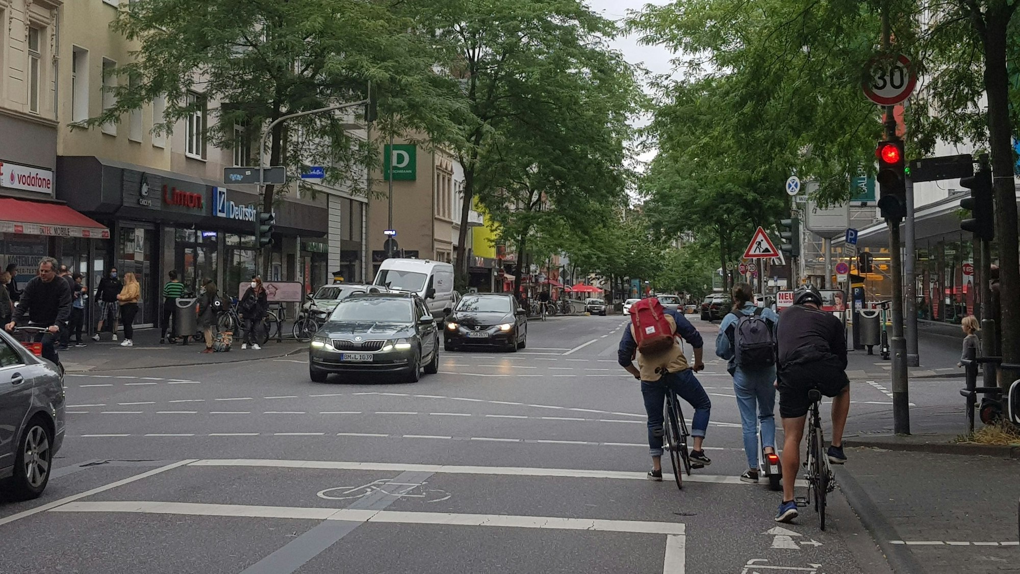 Eine Szene auf der Neusser Straße mit Fahrradfahrenden und Autos an einer Ampel.