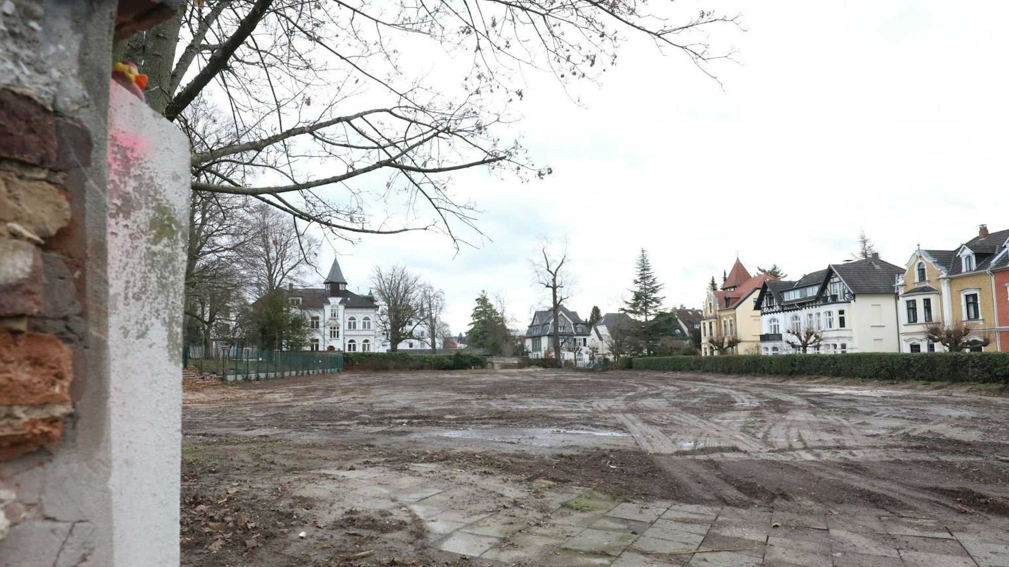 Neben einem Stück abgebrochener Mauer liegt eine große leere Fläche mit nacktem Boden. Rechts im Hintergrund sind alte Jugendstil-Villen zu sehen, die das Stadtbild in der Königin-Sophie-Straße prägen.