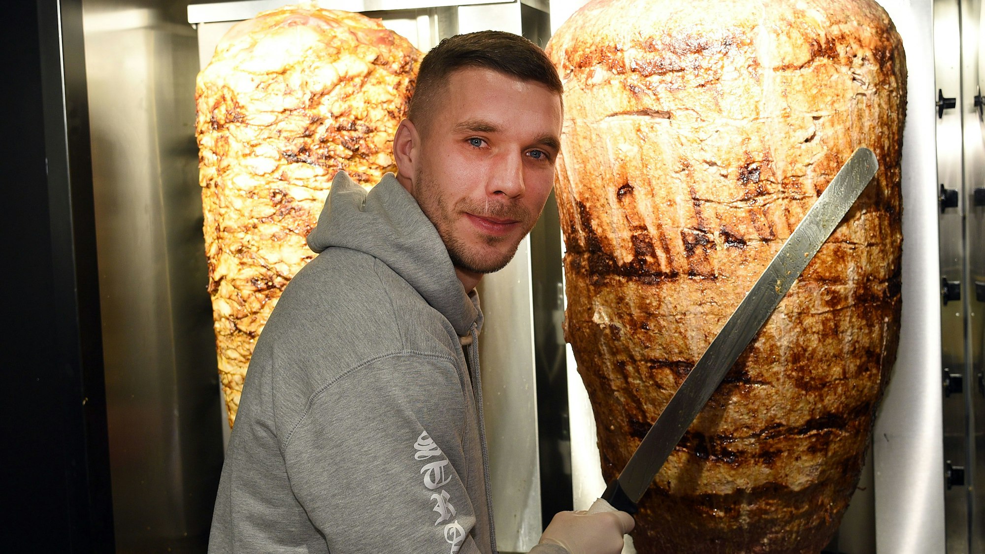 Fußball-Weltmeister Lukas Podolski steht am 06.01.2018 in Köln bei der Eröffnung eines Döner-Ladens an einem Dönerspieß. Podolski ist Mitgesellschafter bei „Mangal Döner“.
