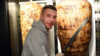 Lukas Podolski steht bei der Eröffnung eines Döner-Ladens an einem Dönerspieß.