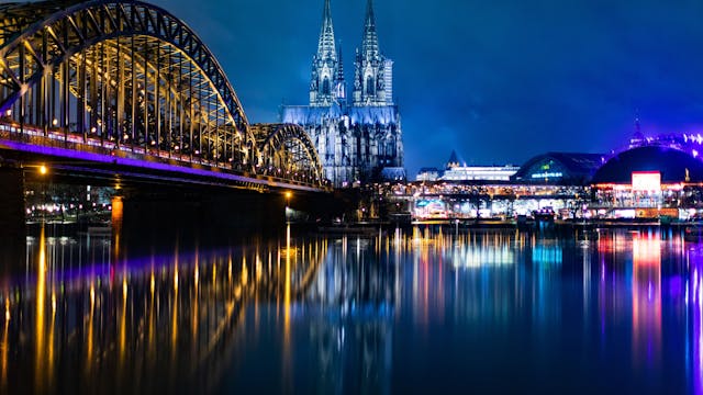 Die bunt beleuchtete Hohenzollernbrücke mit dem Kölner Dom und dem Musical Dome bei Nacht.