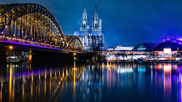 Die bunt beleuchtete Hohenzollernbrücke mit dem Kölner Dom und dem Musical Dome bei Nacht.