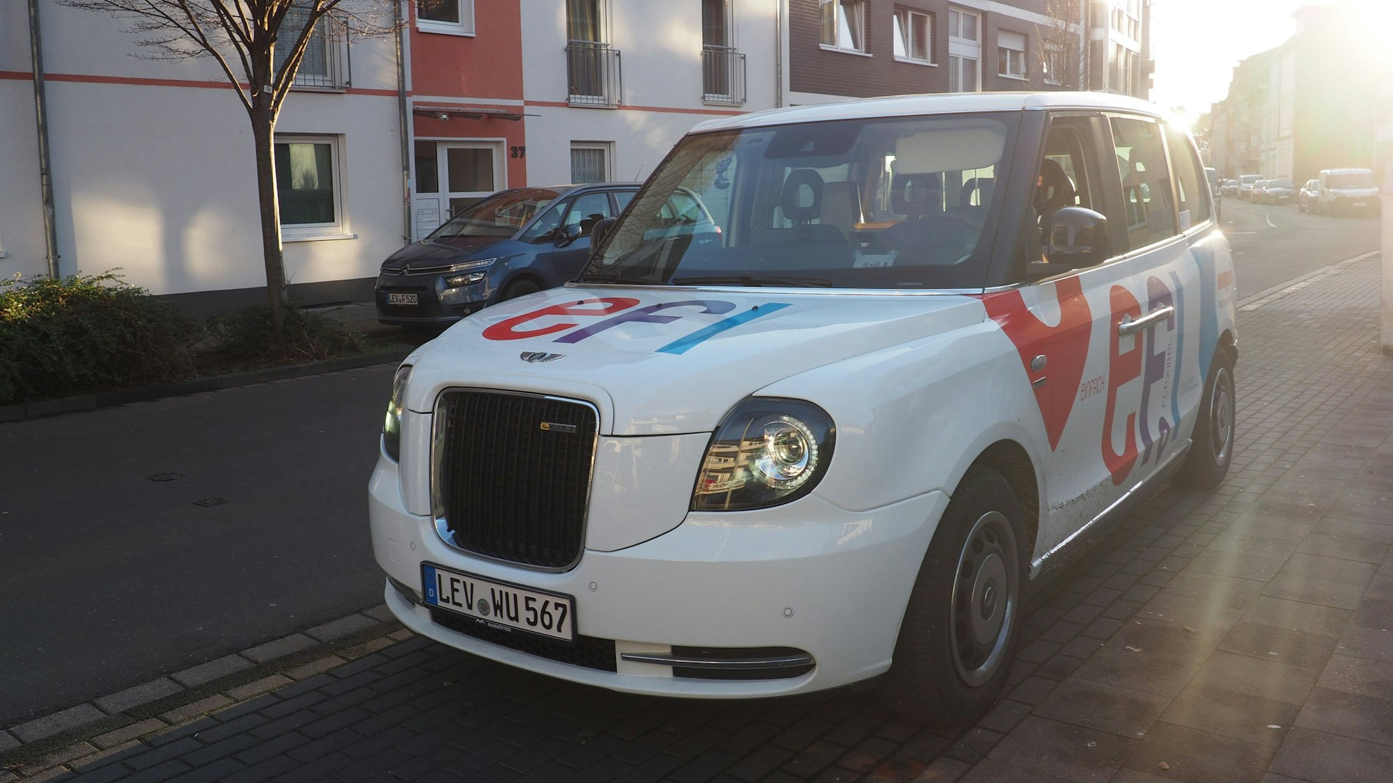 Ein weißes Auto in Form der Londoner Taxen mit der Aufschrift „Efi“ in der Birkenbergstraße.