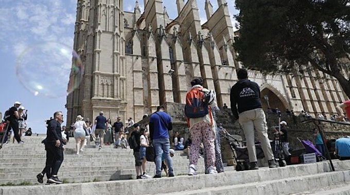 Menschen gehen neben der Kathedrale von Palma de Mallorca spazieren.