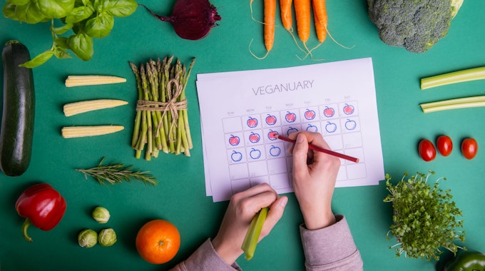 Jemand füllt einen Veganuary-Plan aus, darum liegt verschiedenen Obst und Gemüse.