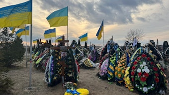 Ukrainischen Flaggen und Berge von Blumen auf den Gräbern der gefallenen Soldaten auf dem Friedhof in Butscha.