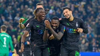 Manu Koné, Marcus Thuram und Ramy Bensebaini jubeln, lachen und liegen sich nach einem Tor im Bundesliga-Spiel gegen Borussia Dortmund am 11. November 2022 in den Armen. Die drei Gladbach-Spieler tragen schwarze Trikots und schwarze Hosen.