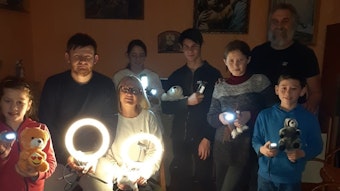 Ein Ehepaar, Paul Kruk und fünf Waisenkinder, die von der Familie aufgenommen wurden, stehen mit Lichtern in einem dunklen Raum.