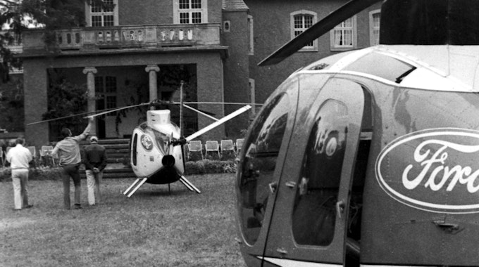 Zwei Hubschrauber mit Ford-Logos steht vor der Burg Dalbenden, daneben drei von der Kamera abgewandte Personen. Das Foto ist in schwarz-weiß.