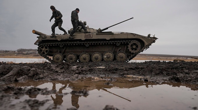 Zwei ukrainische Soldaten stehen während einer Schießübung auf einem Panzer, der auf einem Feld voller Pfützen steht.