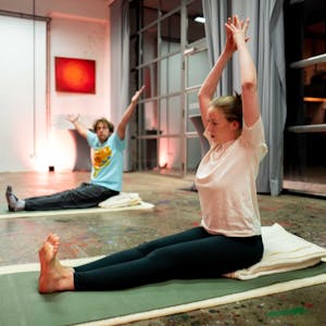 Tom Steinicke und Stella Wolters sitzen auf Yoga-Matten und machen eine Übung.