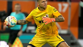 Torwart Rafal Gikiewicz vom FC Augsburg, hier beim Bundesliga-Spiel gegen den VfL Bochum am 12. November 2022, macht im gelben Trikot einen Abwurf.