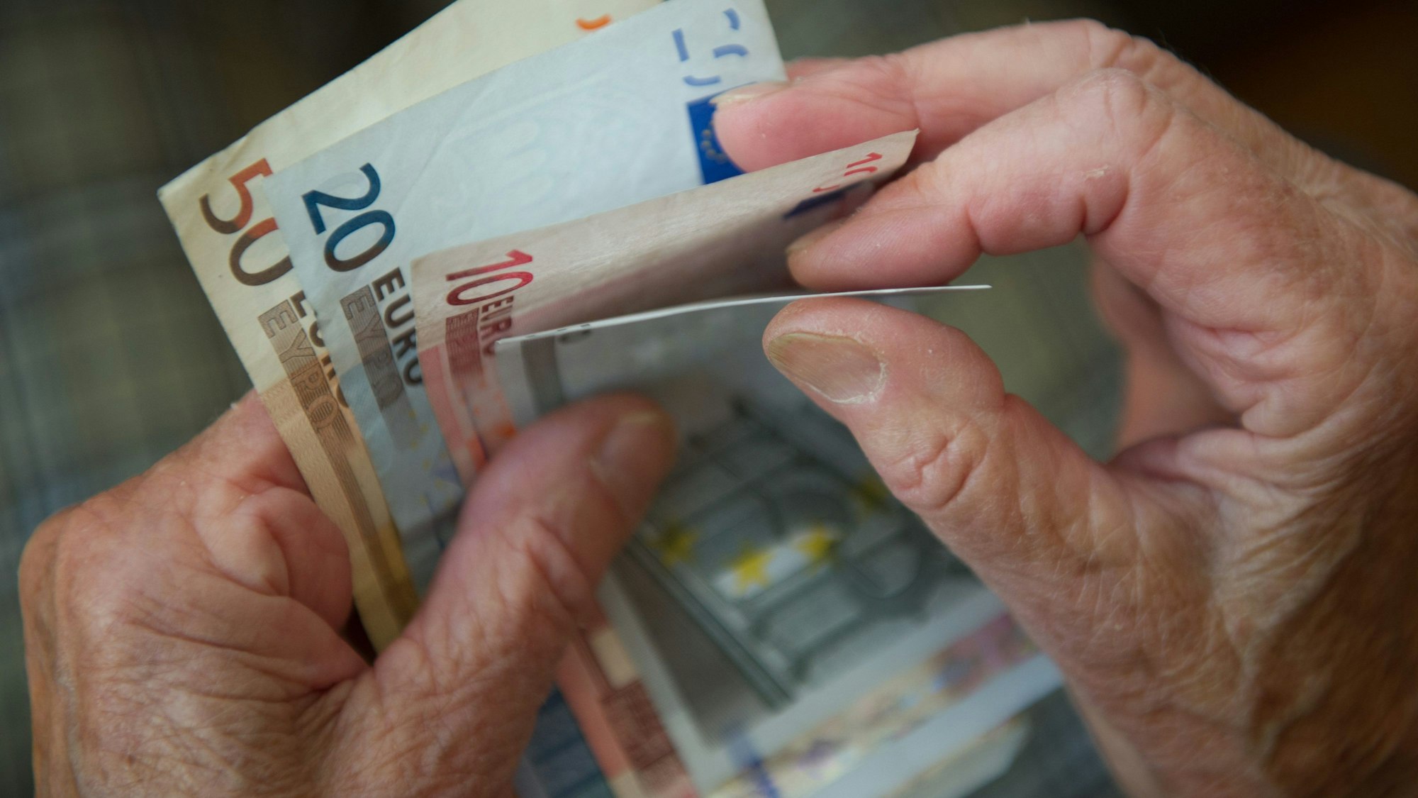 Eine ältere Person hält verschiedene Geldscheine in den Händen. Zu sehen sind 50, 20, zehn und fünf Euro-Scheine.