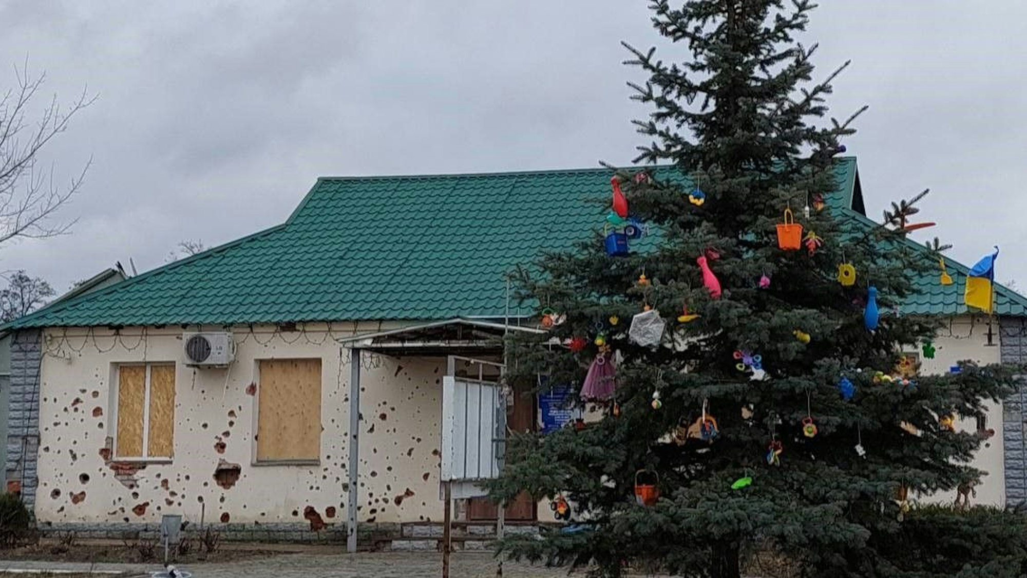 Ein mit Kinderspielzeug geschmückter Baum steht vor einem kaputten Haus.