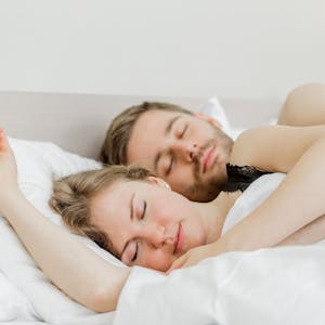 Eine Frau und ein Mann liegen aneinandergekuschelt im Bett und schlafen.
