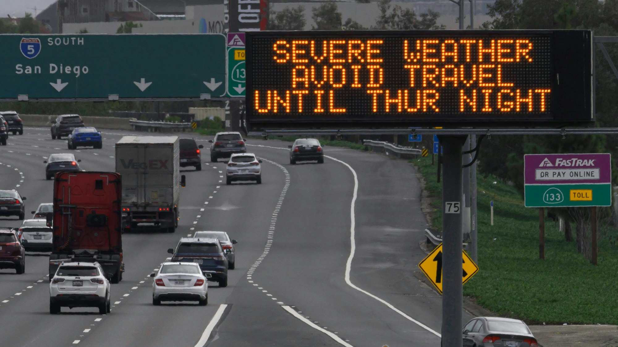 Ein Schild entlang der Interstate 5 warnt Autofahrer vor einem bevorstehenden Unwetter in Kalifornien. Mehrere Autos fahren über die Autobahn.