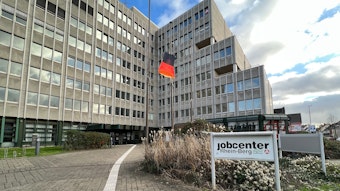 Ein Schild mit der Aufschrift „Jobcenter“ steht vor einem Hochhaus. In dem Hochhaus findet sich das Jobcenter Rhein-Berg.