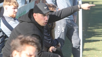 Trainer Sebastian Korthaus ruft aufs Spielfeld und gibt mit ausgestrecktem Arm und Zeigefinger die Richtung vor.