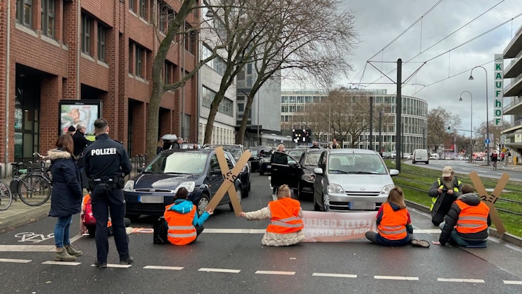 Aktivistinnen und Aktivisten der „Letzten Generation“ blockieren am Freitagmittag mit einer Sitzblockade eine der zentralen Verkehrsachsen in der Kölner Innenstadt.