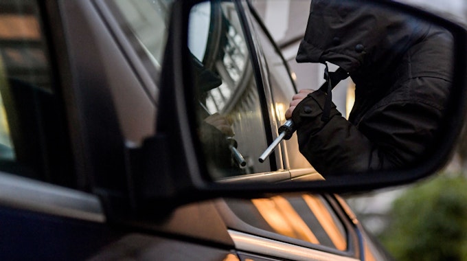 Das gestellte Foto zeigt einem Mann, der versucht, eine Autotür mit einer Metallstange aufzubrechen.