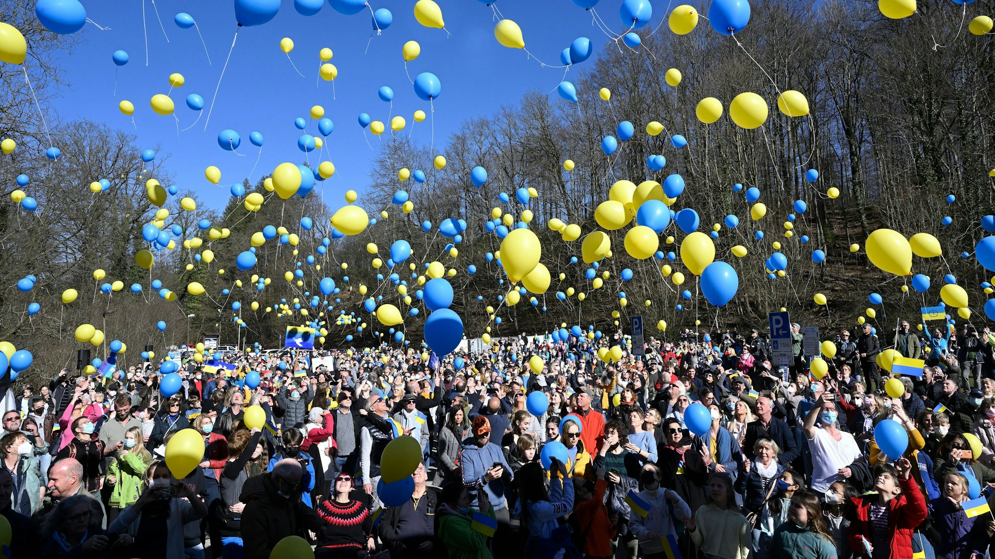Hunderte Menschen lassen gelbe und blaue Luftballons in die Luft steigen.