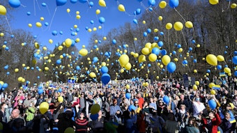 Hunderte Menschen lassen gelbe und blaue Luftballons in die Luft steigen.