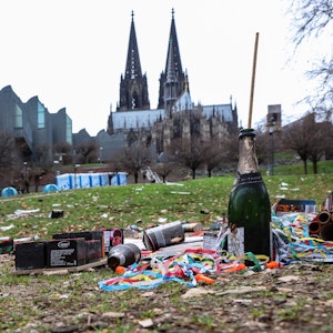 Müll liegt nach Silvester im Rheingarten in Köln. Im Hintergrund ragt der Kölner Dom hervor.