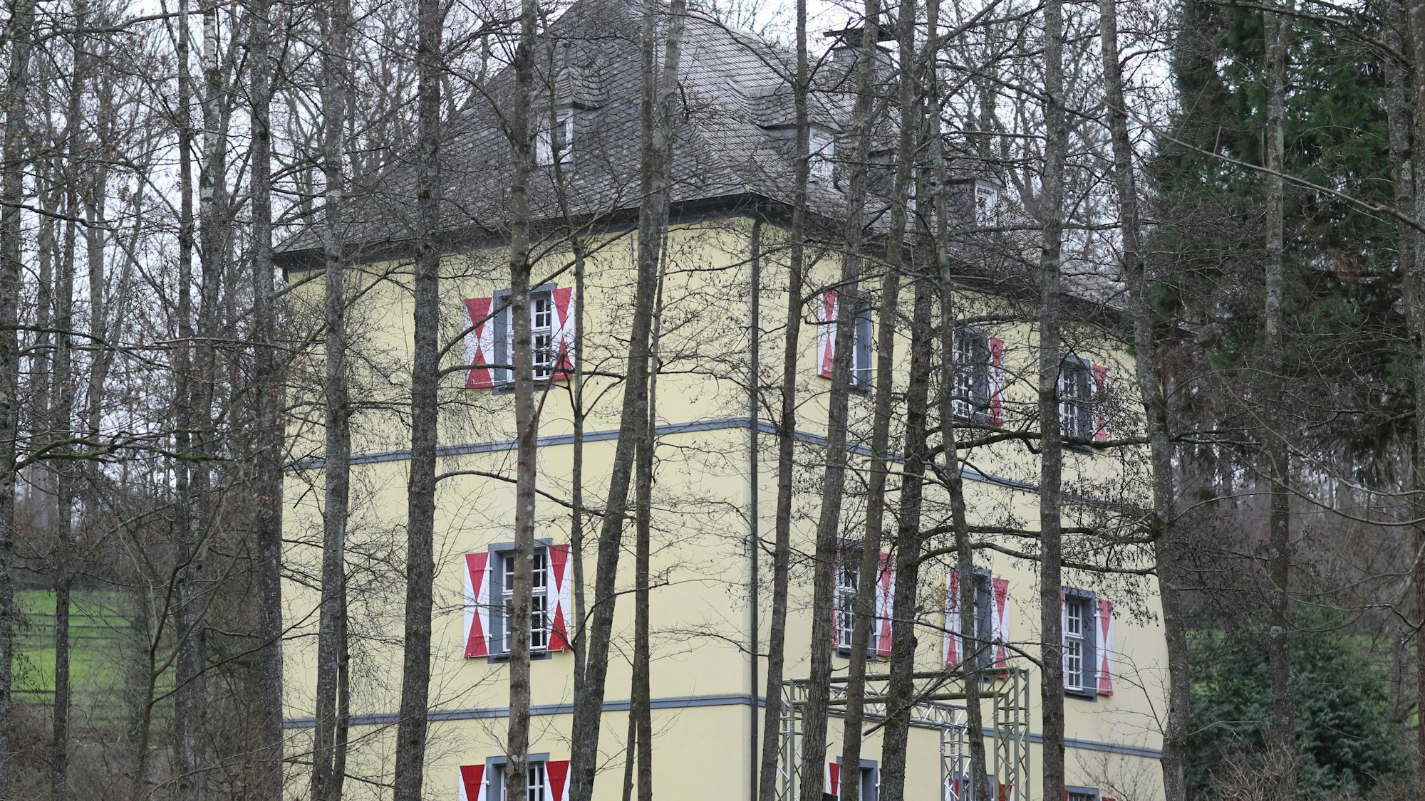 Die Burg Welterode in Eitorf mit gelber Fassade und weiß-roten Fensterläden, umringt von Bäumen.
