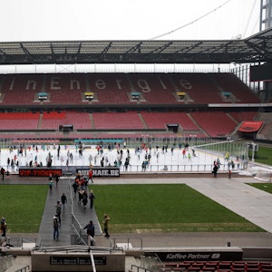 Auf der Eisfläche, die im Rheinenergie-Stadion aufgebaut ist, laufen viele Menschen mit ihren Schlittschuhen. Dahinter ist die leere Tribüne zu sehen.