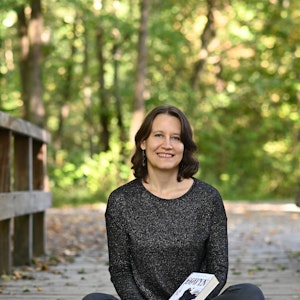 Elvira Zeißler sitzt mit einigen ihrer Bücher auf dem Schoß auf einem Holzsteeg.