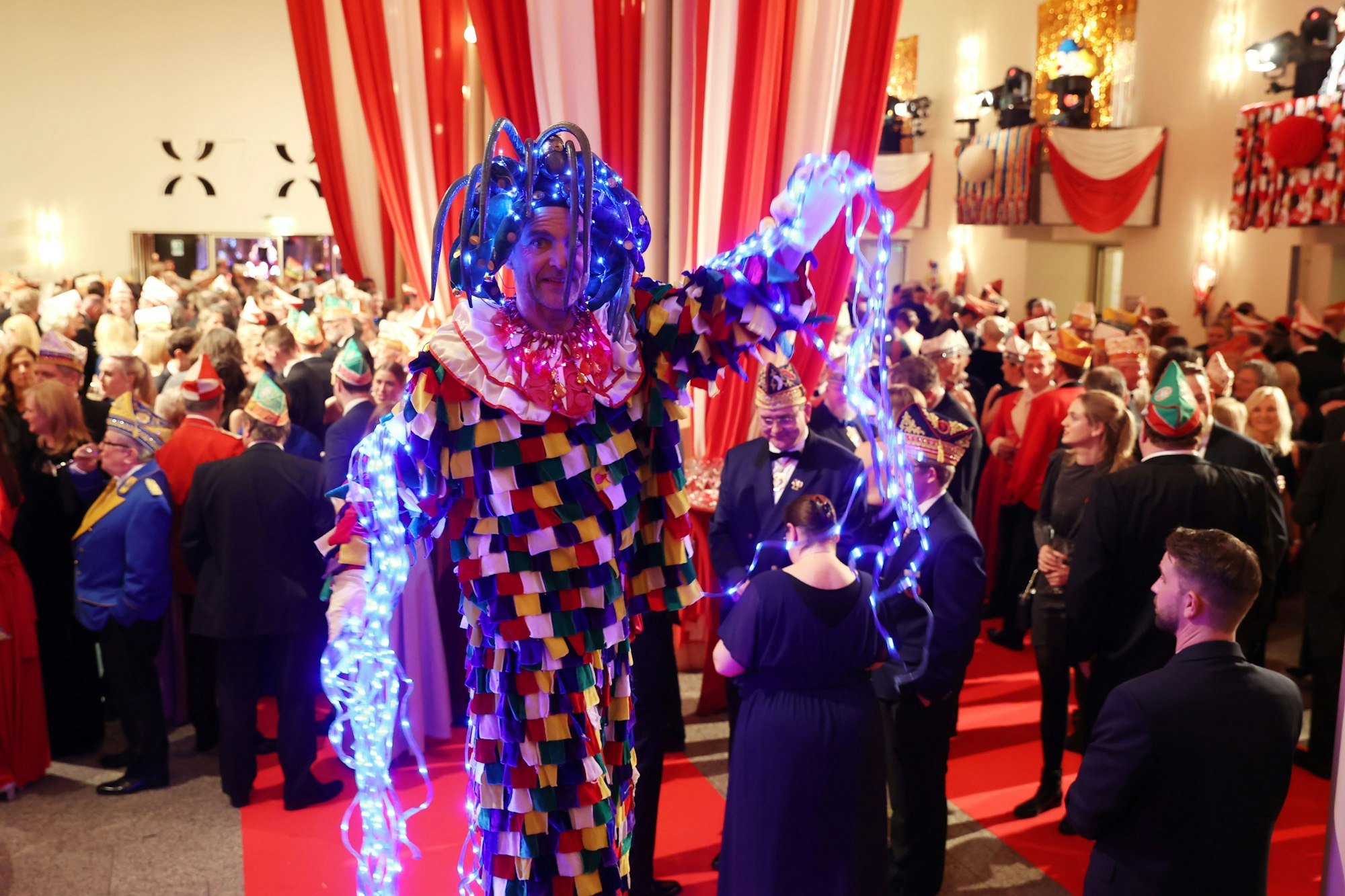 Ein Man in bunt-leuchtendem Kostüm steht in der Menge der Prinzenproklamations-Gäste.