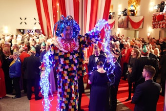 Ein Man in bunt-leuchtendem Kostüm steht in der Menge der Prinzenproklamations-Gäste.