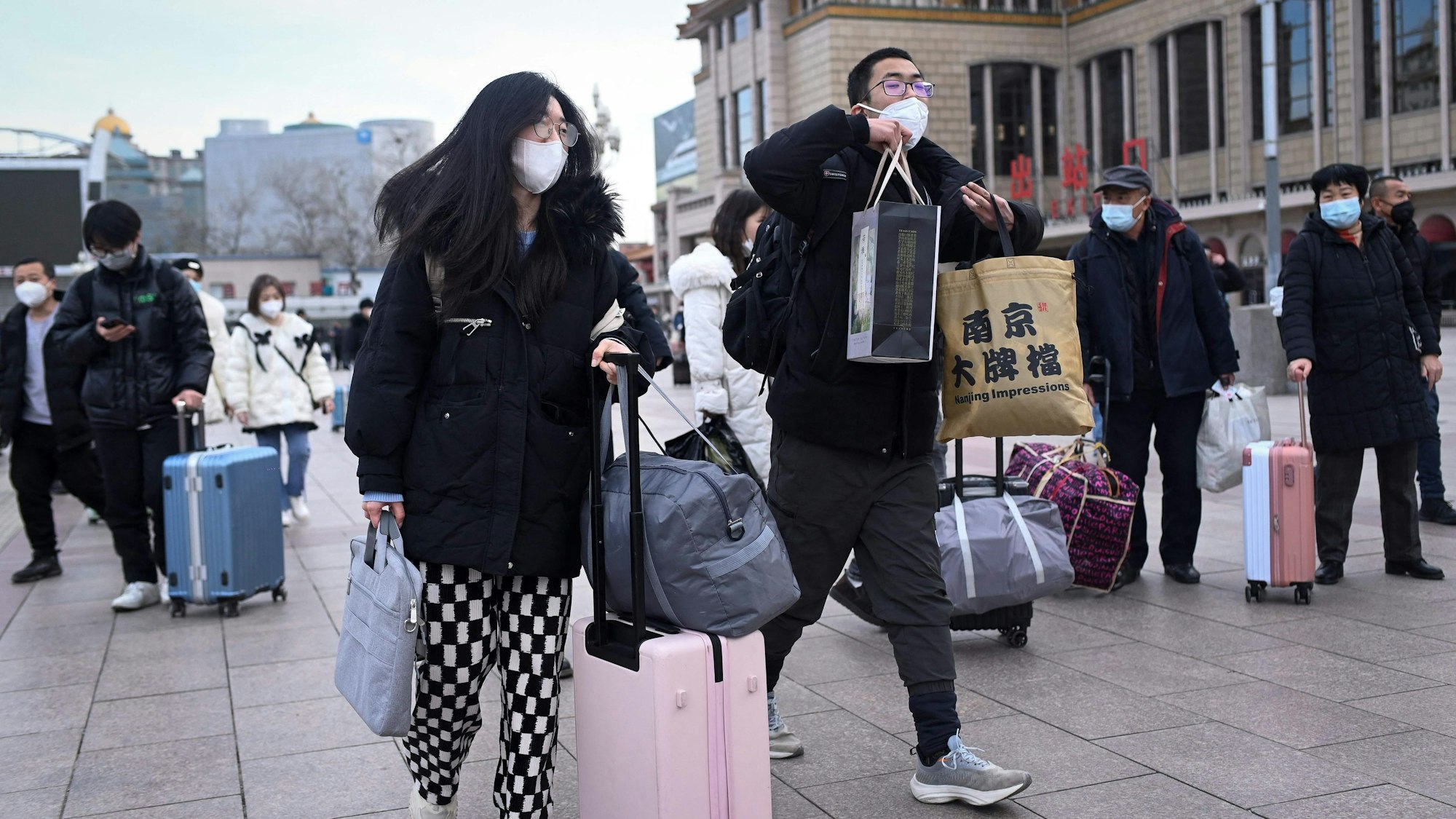 Menschen tragen Koffer und Taschen und haben Gesichtsmasken an.