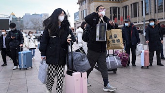 Menschen tragen Koffer und Taschen und haben Gesichtsmasken an.