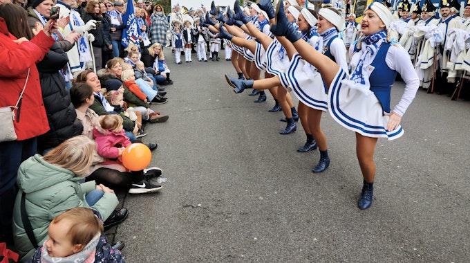 Die Mädchen- und Frauengarde der Opladener Altstatfunken tanzt auf der rechten Seite und hat die Beine in der Luft, links schauen Familien dem Treiben zu.
